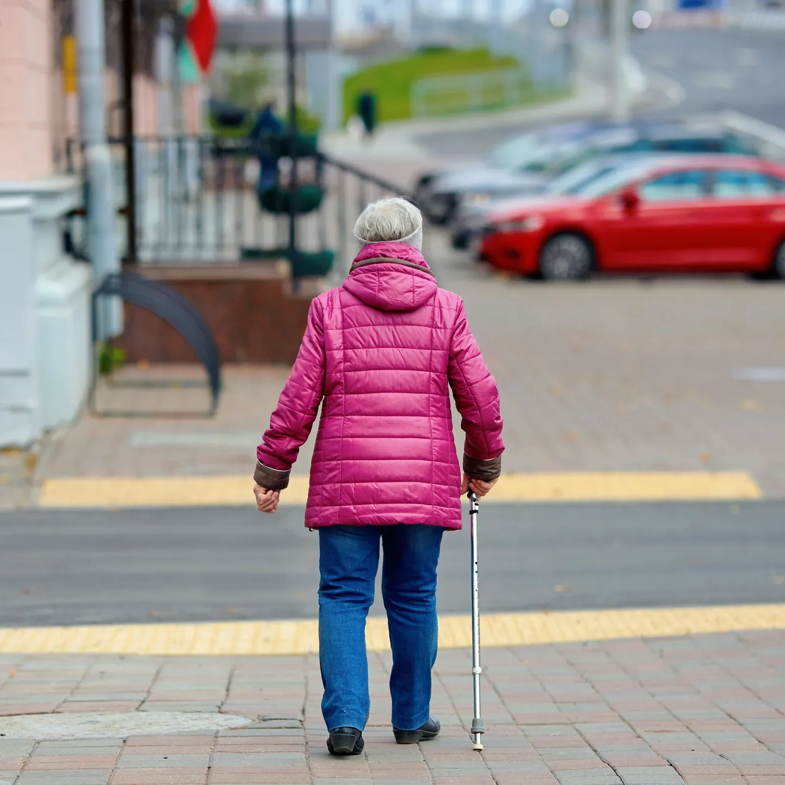 An older woman with a cane walks toward a street crossing.