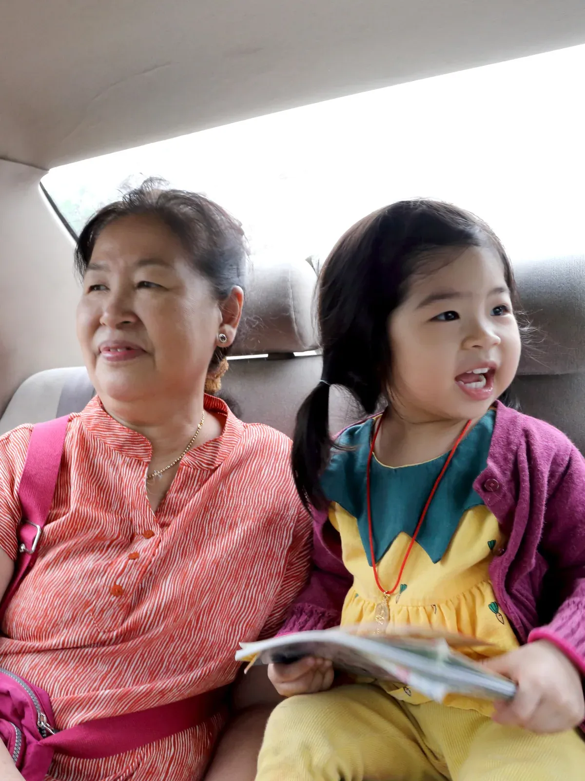 An older woman and a little girl smile in the back seat of a car.