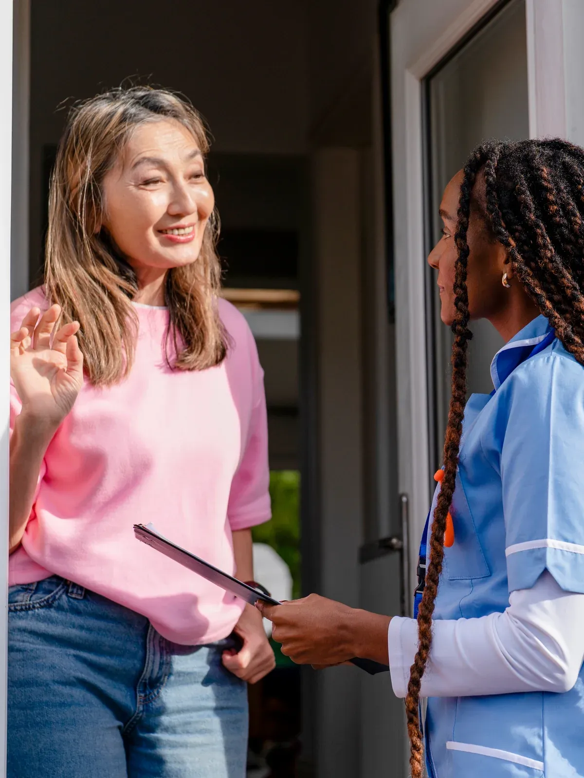 A home health aide talks with a woman at her front door.