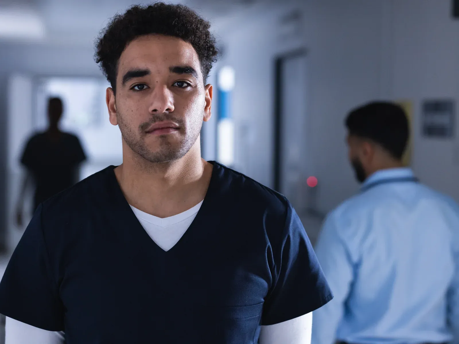 A hospital worker in scrubs stands in a hallway.