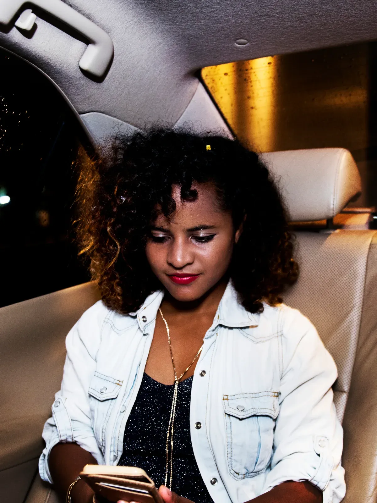 A woman checks her phone in the back seat of a car at night.