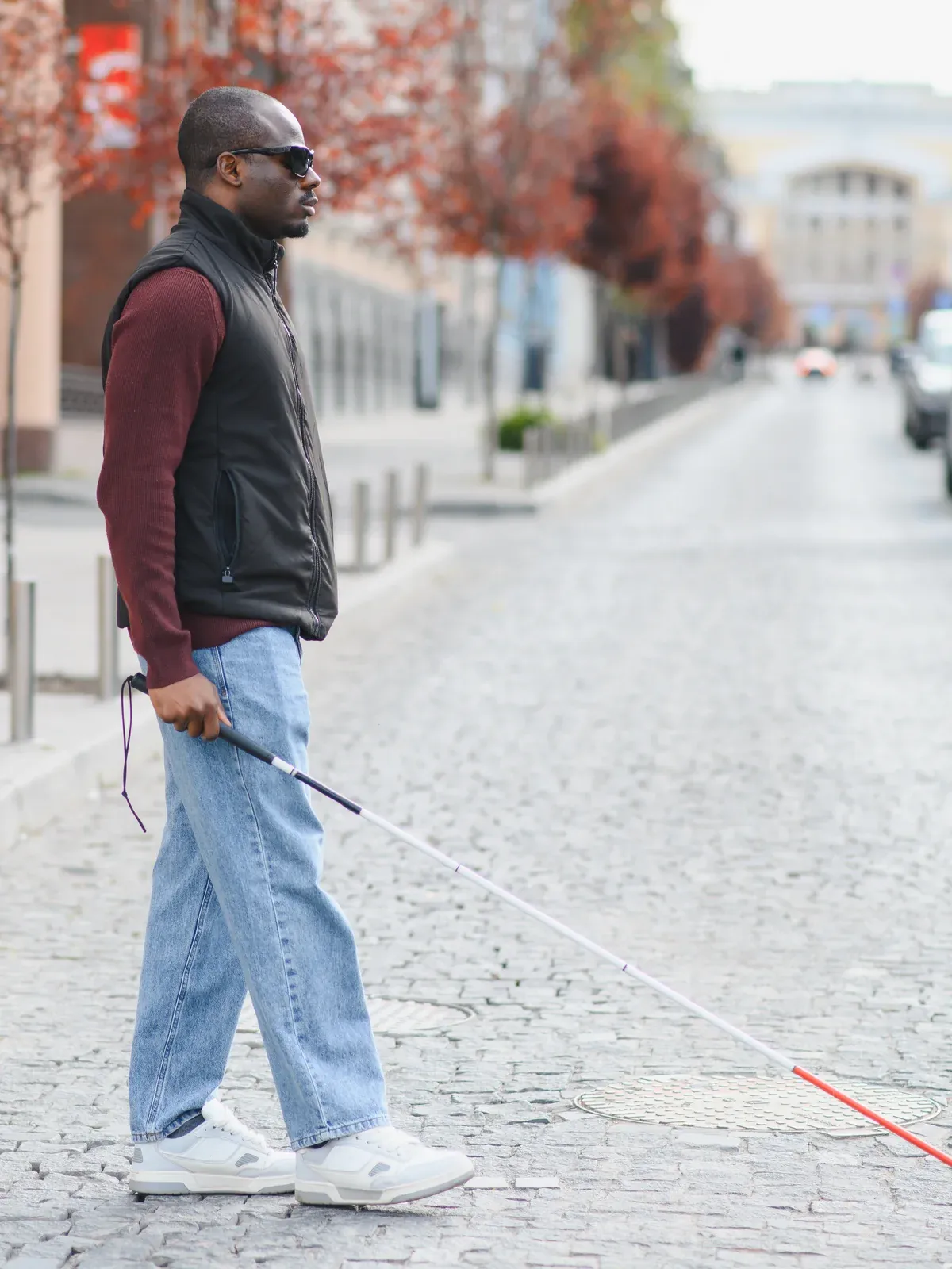 A man using a white cane crosses a city street.